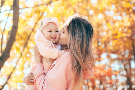 A womans mother holds a baby girl in her arms on a walk in an autumn park.