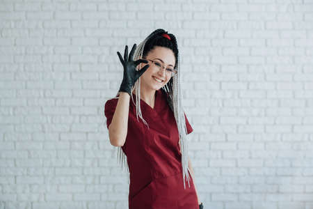 young woman with African braids on her head in a red medical uniform and black gloves folded her fingers in the shape of a heart. expresses confidence and looks into the frame.の写真素材