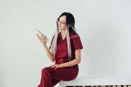 a young woman wearing a red medical uniform and holding a bottle of cream with a care product is...