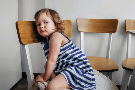 child girl sitting on a chair and looking sadly at the camera.の写真素材