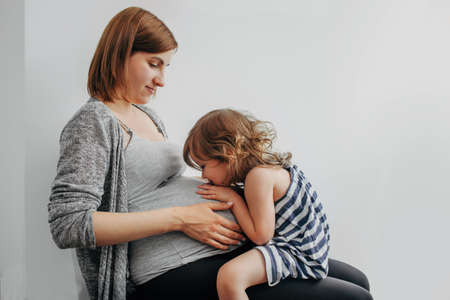 child girl sitting on the legs of a pregnant mother and communicating with the child in the womans tummyの写真素材