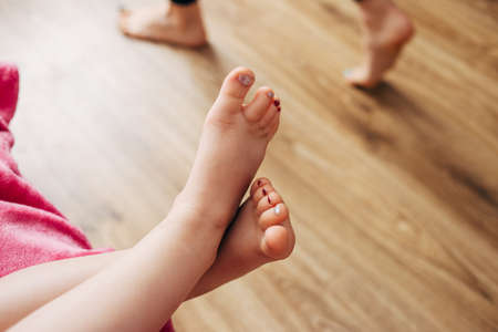 childrens legs with painted nails on a background of brown parquet.の写真素材