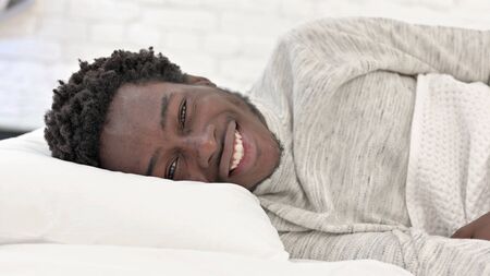 Smiling Young African Man Lying in Bed on Side
