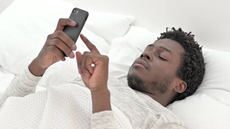 African Man Scrolling is Smartphone in bed