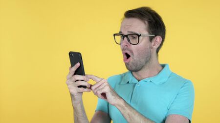 Casual Man Excited for Success while Using Smartphone Isolated on Yellow Backgroundの写真素材