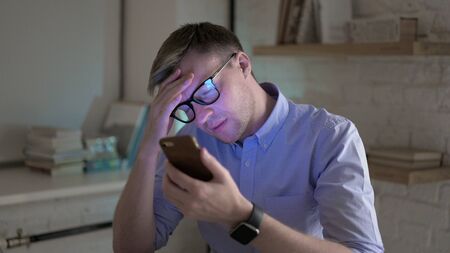 Upset Businessman with Headache Using Smartphoneの写真素材