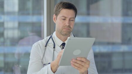 Middle Aged Doctor Scrolling on Tablet, Using Internetの写真素材