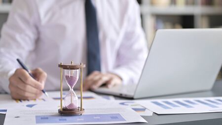 Close Up of Hourglass on Desk and Businessman working on Laptopの写真素材