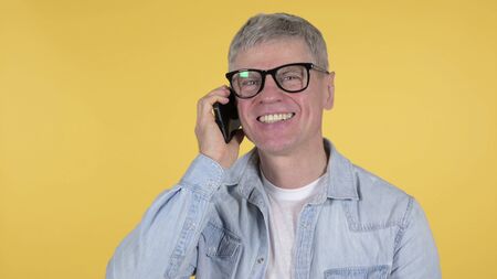 Casual Old Man Talking on Smartphone on Yellow Background