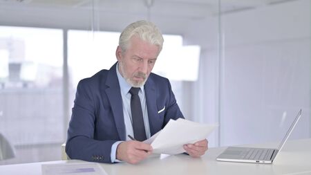 Old Businessman Reading Documents in Officeの写真素材