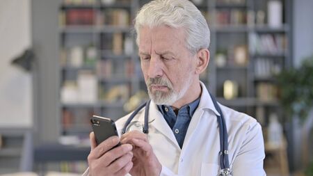 Portrait of Professional Senior Old Doctor using Smartphone