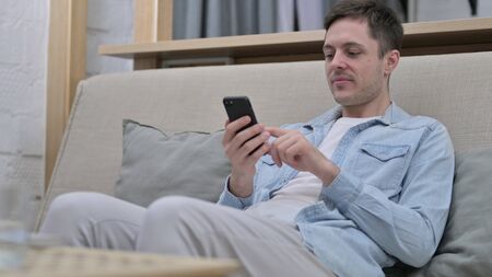 Relaxed Young Man using Smartphone in Living Roomの写真素材