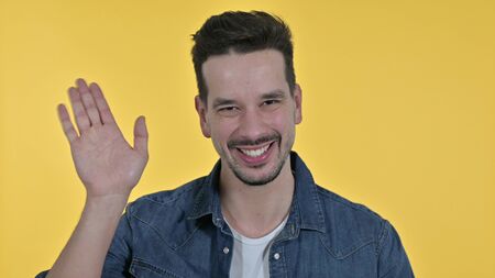 Young Man Waving at the Camera, Yellow Backgroundの写真素材