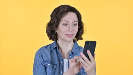 Old Woman using Smartphone on Yellow Backgroundの写真素材