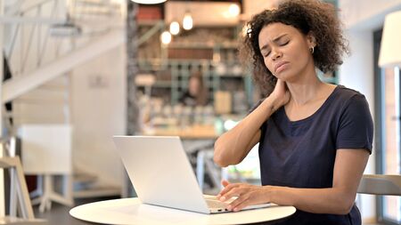 Young African Woman with Neck Pain using Laptop in Cafeの写真素材