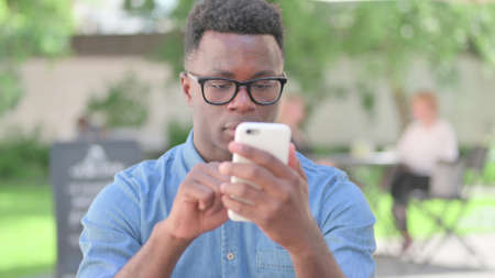 Outdoor African Man Browsing Internet on Smartphoneの写真素材