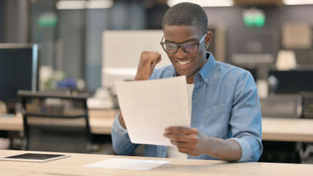 Young African Man Celebrating While Reading Documentsの写真素材