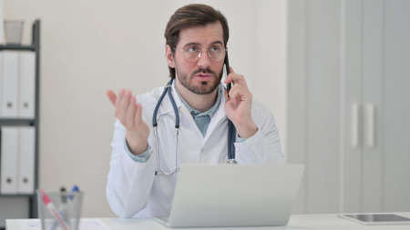 Young Doctor with Laptop Talking on Phoneの写真素材