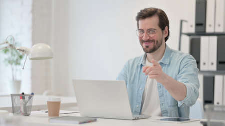 Young Man with Laptop Pointing at Cameraの写真素材