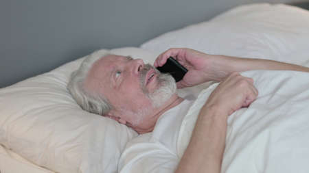 Senior Old Man Talking on Phone Laying in Bedの写真素材