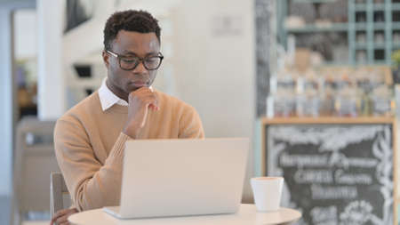 African Man Thinking while using Laptop in Cafe
