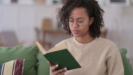 Young African Woman Sitting Reading Book at Home
