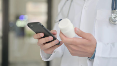 Close up of Doctor Using Smartphone while Holding Medicineの写真素材