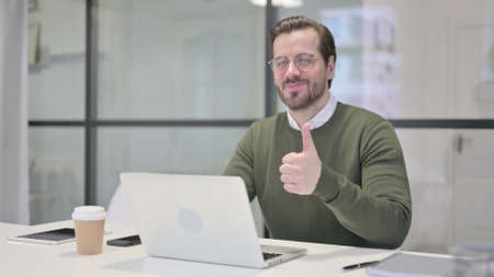 Young Businessman Showing Thumbs Up While using Laptop in Officeの写真素材