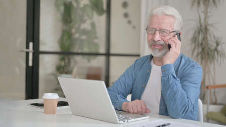 Senior Old Man Talking on Phone while using Laptop