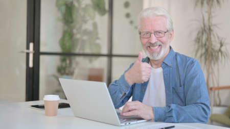 Senior Old Man showing Thumbs Up while using Laptop in Officeの写真素材