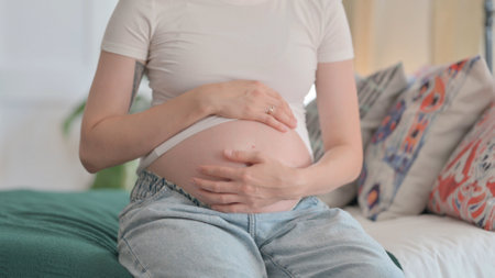 Pregnant Woman Stokes Her Big Belly after Removing Shirt, Close Upの写真素材