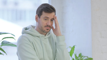 Young Adult Man with Headache, Migraine while Standing Near Windowの写真素材