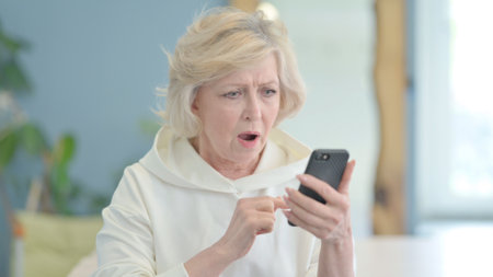 Portrait of Mature Adult Woman Shocked by Loss on Smartphoneの写真素材