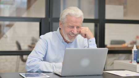 Old Businessman Chatting Online on Laptop while Sitting in Office