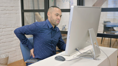 Hispanic Businessman having Back Pain while Working on Desktop