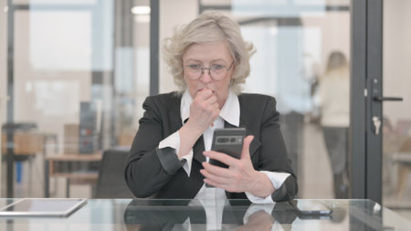 Senior Businesswoman Shocked by Loss on Phoneの写真素材