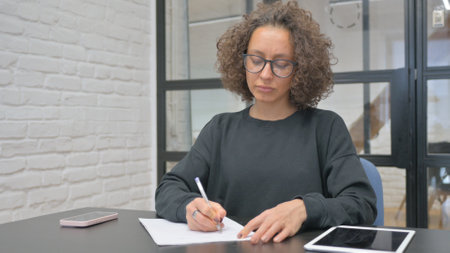 Hispanic Woman Writing while at Workの写真素材