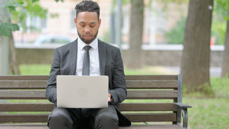 Man Looking at Camera while Using Laptop Outdoorの写真素材