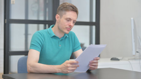 Casual Young Man Reading Documents in Office