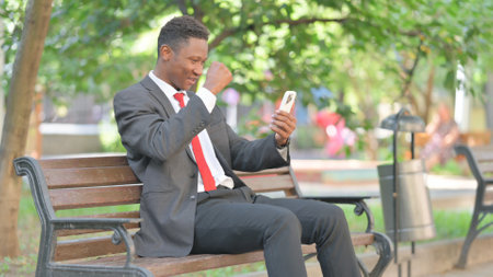 African Businessman Celebrating Success on Phone Outdoorの写真素材
