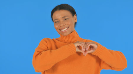 Casual African Woman Making Heart Sign with Hands on Blue Backgroundの写真素材