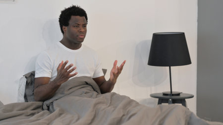 Young african american man sitting in bed.の写真素材