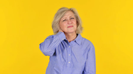 Senior woman suffering from neck pain on yellow background. Health care concept