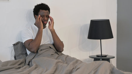 African Man having Migraine while Sitting in Bed