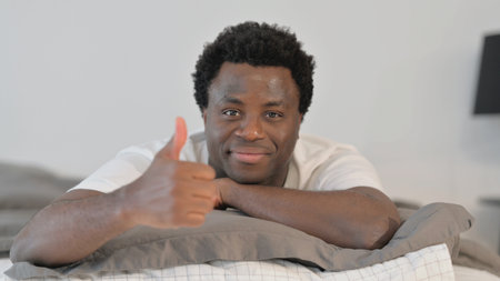 Thumbs Up by African Man Lying on Stomach in Bed