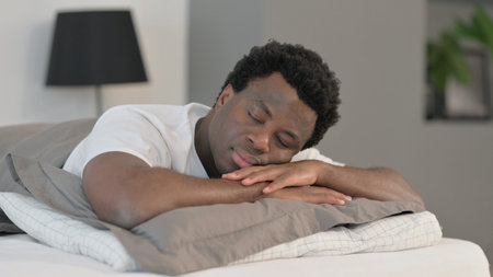 Sleeping African Man while Lying on Stomach in Bedの写真素材