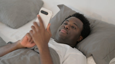 African Man Using Smartphone while Lying in Bed