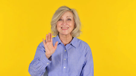 Old Woman Waving Hand to Welcome on Yellow Background, Portrait