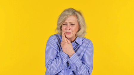 Old Woman with Tooth Pain on Yellow Background, Portraitの写真素材
