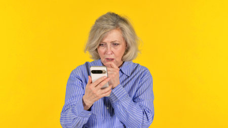 Old Woman Shocked by Loss on Phone on Yellow Background, Portrait